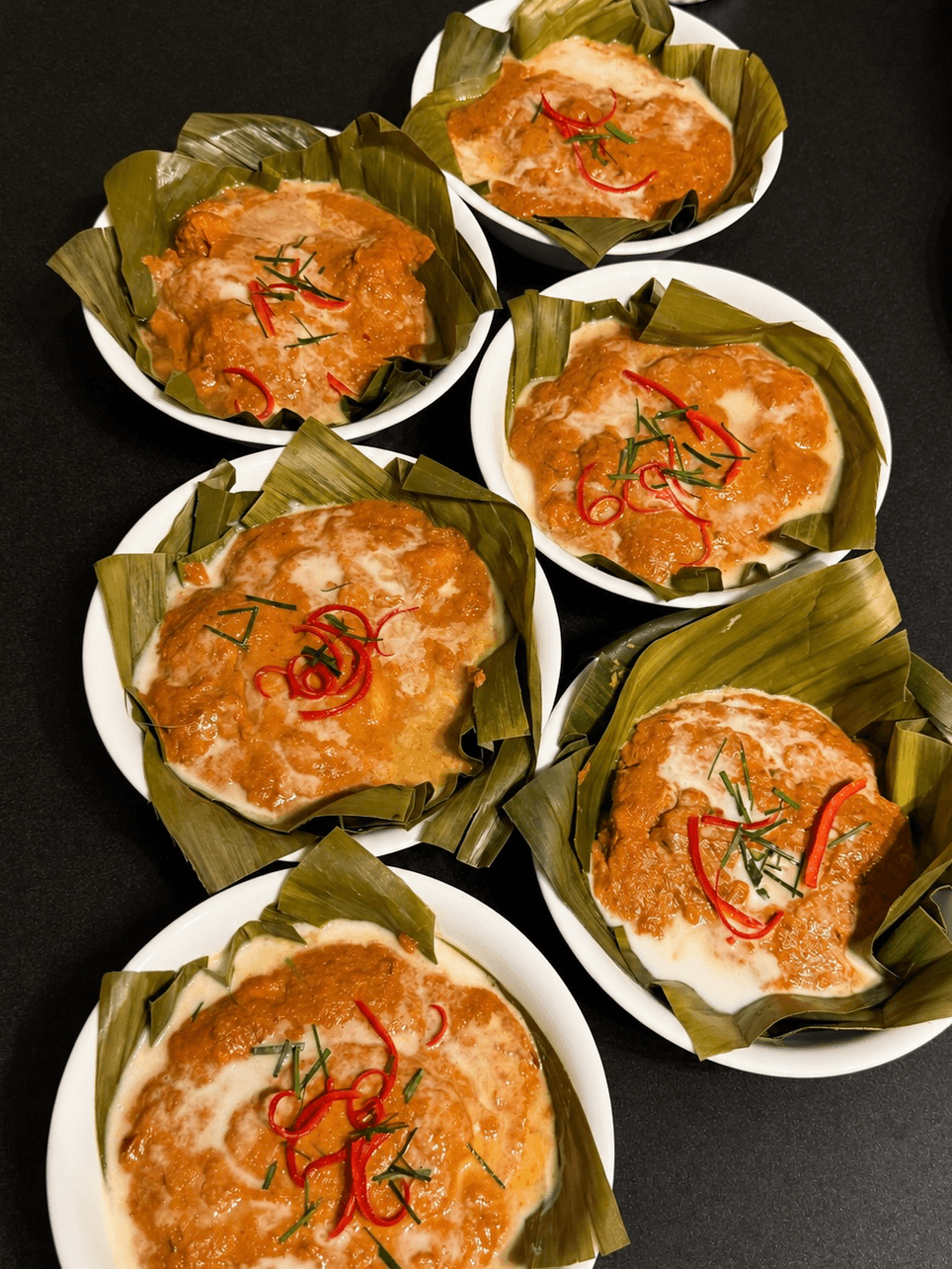 Six bowls of fish amok in banana leaves, topped with coconut cream, chile, and makrut lime
