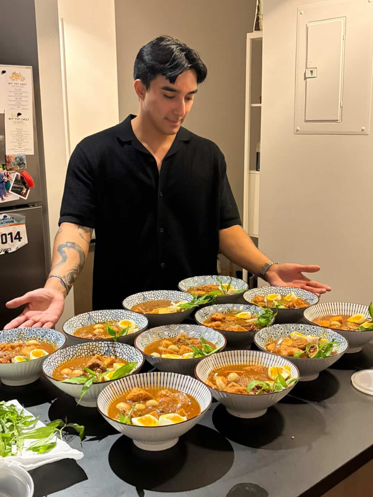 Thet in the kitchen behind a counter of curry laksa bowls ready to go out